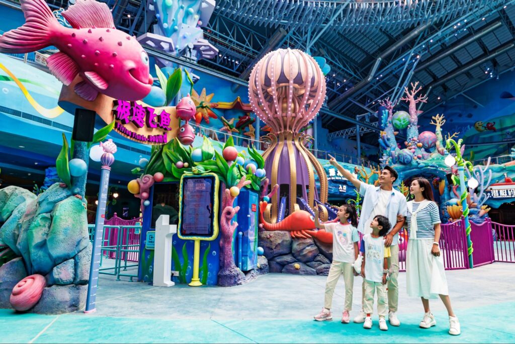 เครื่องเล่น Flying Fish Go-Round ในโซนโลกใต้ทะเลของ Chimelong Spaceship จูไห่ ตกแต่งด้วยปลาสีชมพูขนาดใหญ่และปะการังสีสันสดใส